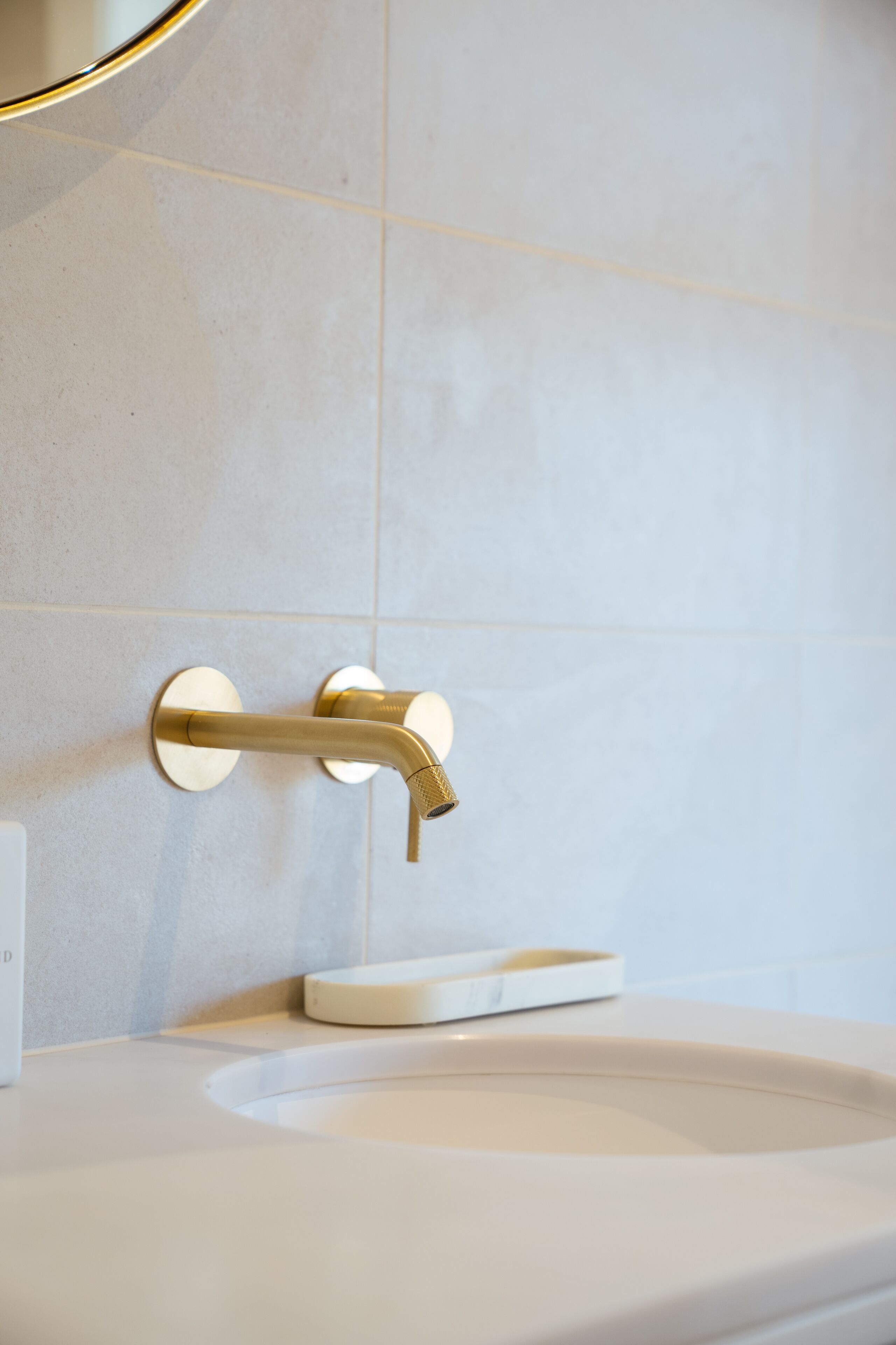 Un baño con lavamanos blanco, grifo dorado y espejo circular en la pared blanca.