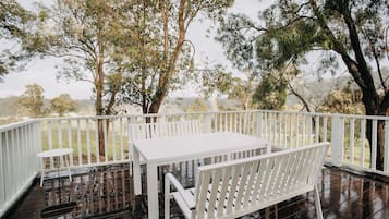 Un espacio al aire libre cubierto con una mesa y banca blancos, rodeado de árboles y una barandilla blanca.