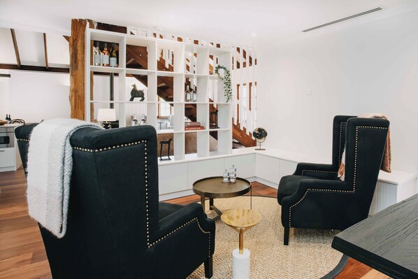 A modern living room with two black armchairs, a round coffee table, and a white shelving unit filled with books and decorative items.