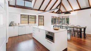 A spacious kitchen with a large island, wooden beams on the ceiling, and a dining area with a table and chairs. - Ampersand Estates (Peerabeelup)