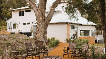 A house with a dirt path leading to a seating area with chairs and a fire pit.