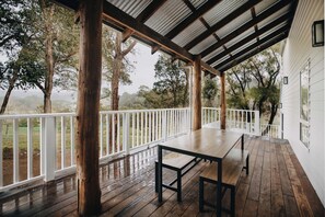 A covered outdoor area with a wooden table and benches, surrounded by white railings and trees. - Ampersand Estates (Peerabeelup)