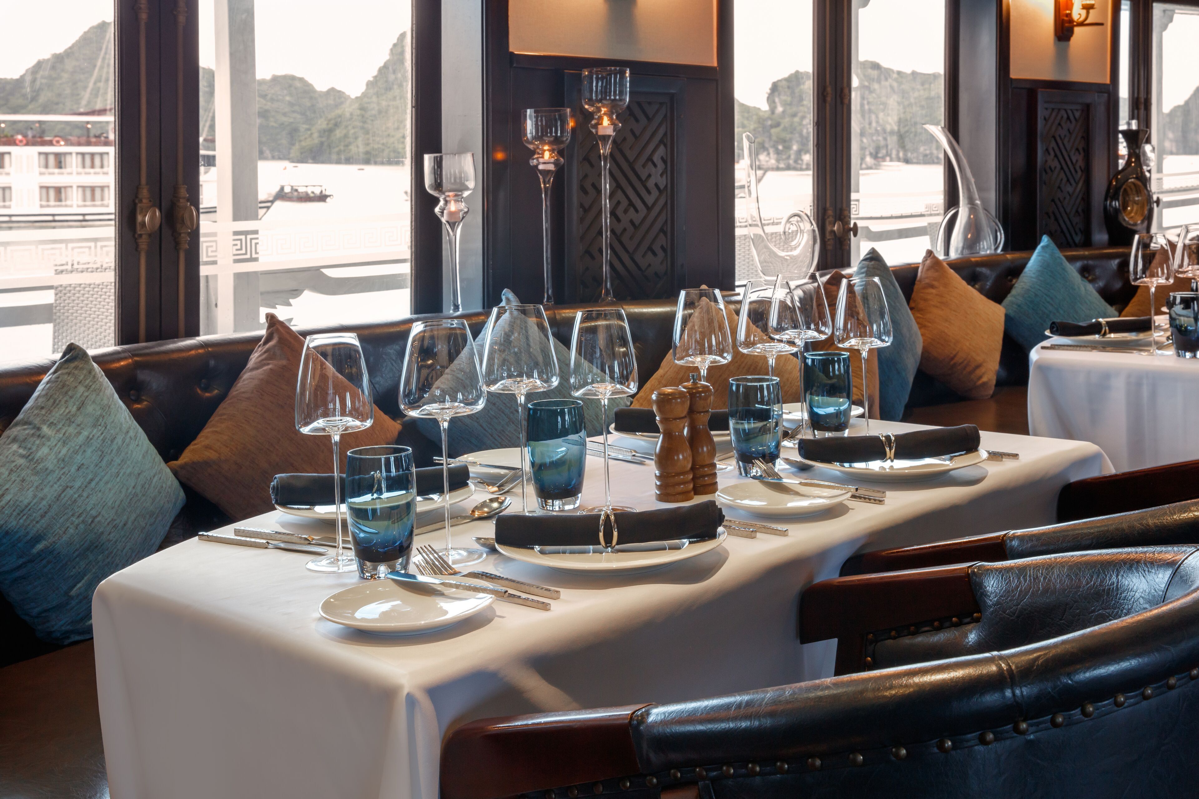 A dining table set with plates, glasses, and cutlery, with a view of a body of water and mountains in the background.