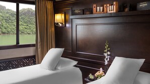 A hotel room with two beds, a nightstand, a lamp, and a shelf with toiletries. - Paradise Sails Cruise Ha Long (Ha Long)