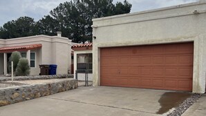 Un garage attenant à une maison, avec une allée en béton, une bordure en pierre et une clôture en métal.