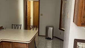 Une cuisine avec un îlot central en bois, une poubelle et un coin repas avec des chaises.