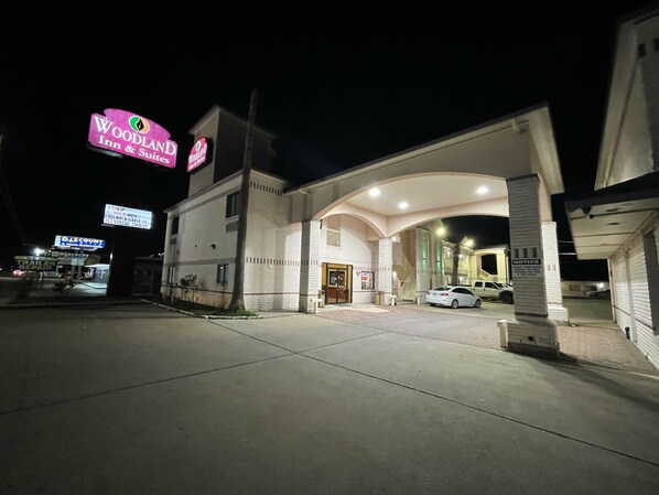 A motel with a large arch entrance, a sign for Woodland Inn & Suites, and a visible car parked in the lot.