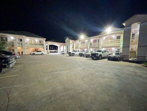 A parking lot with several cars and a building with multiple balconies and a central entrance. - Woodland Inn & Suites (Rosenberg)