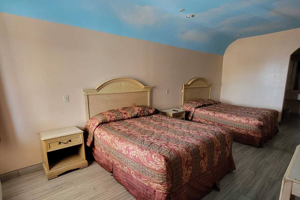A room with two beds, a nightstand, and a ceiling mural.