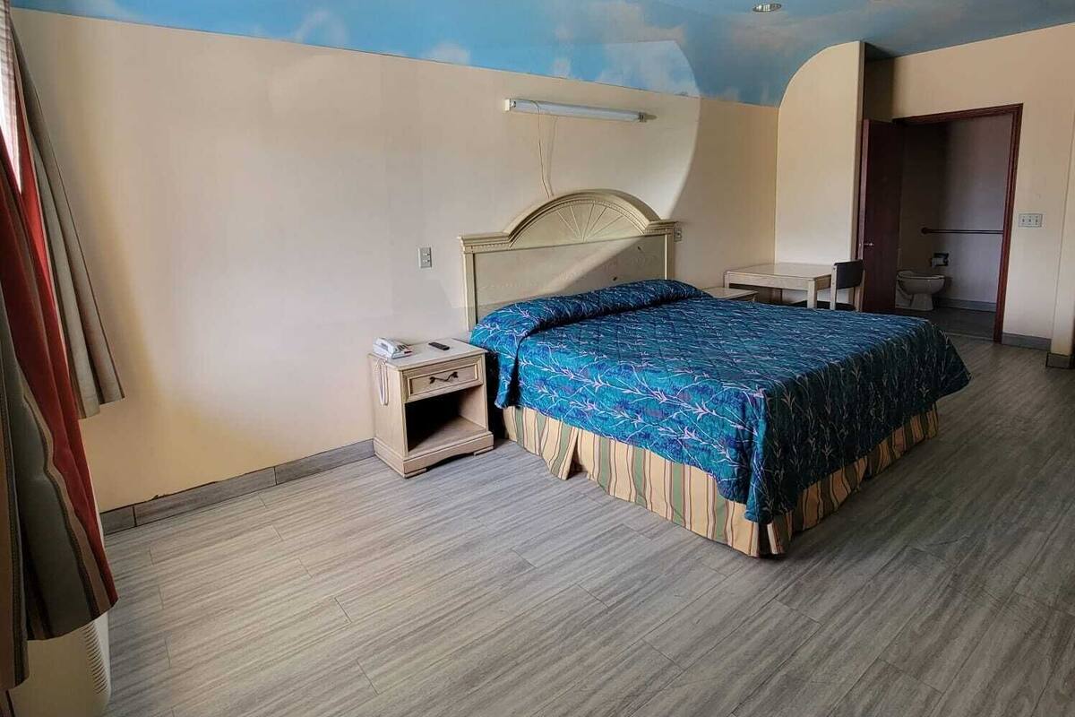 A bedroom with a bed, bedside table, and a ceiling with a cloud design.