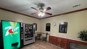 Una cocina con una máquina expendedora de 7UP, un ventilador de techo, un reloj y una planta en maceta.