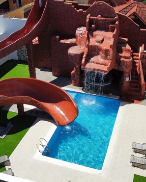 Un parc aquatique avec un toboggan, une piscine et une formation rocheuse.