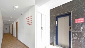 A hotel corridor with a wooden floor, white walls, and a marble wall with a no smoking and no alcohol sign. - UPAR Hotels Uthandi ECR (Chennai)