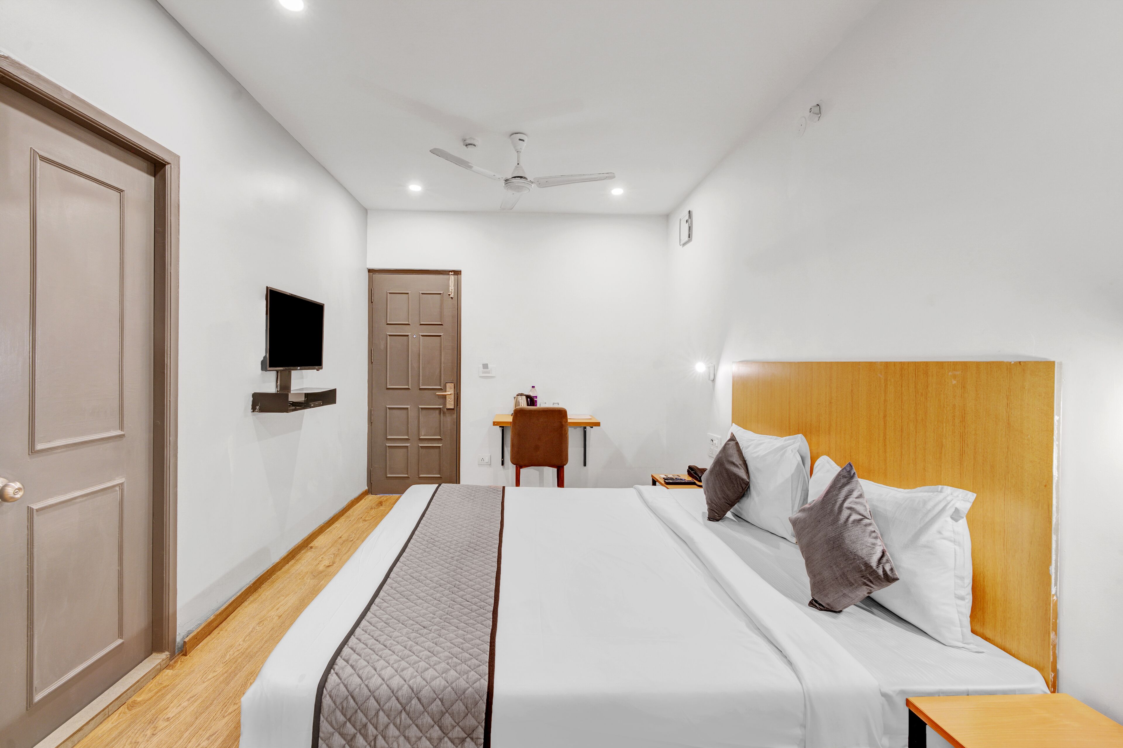 Habitació d'hotel amb un llit, una taula de treball, una cadira, un televisor i un ventilador de sostre.