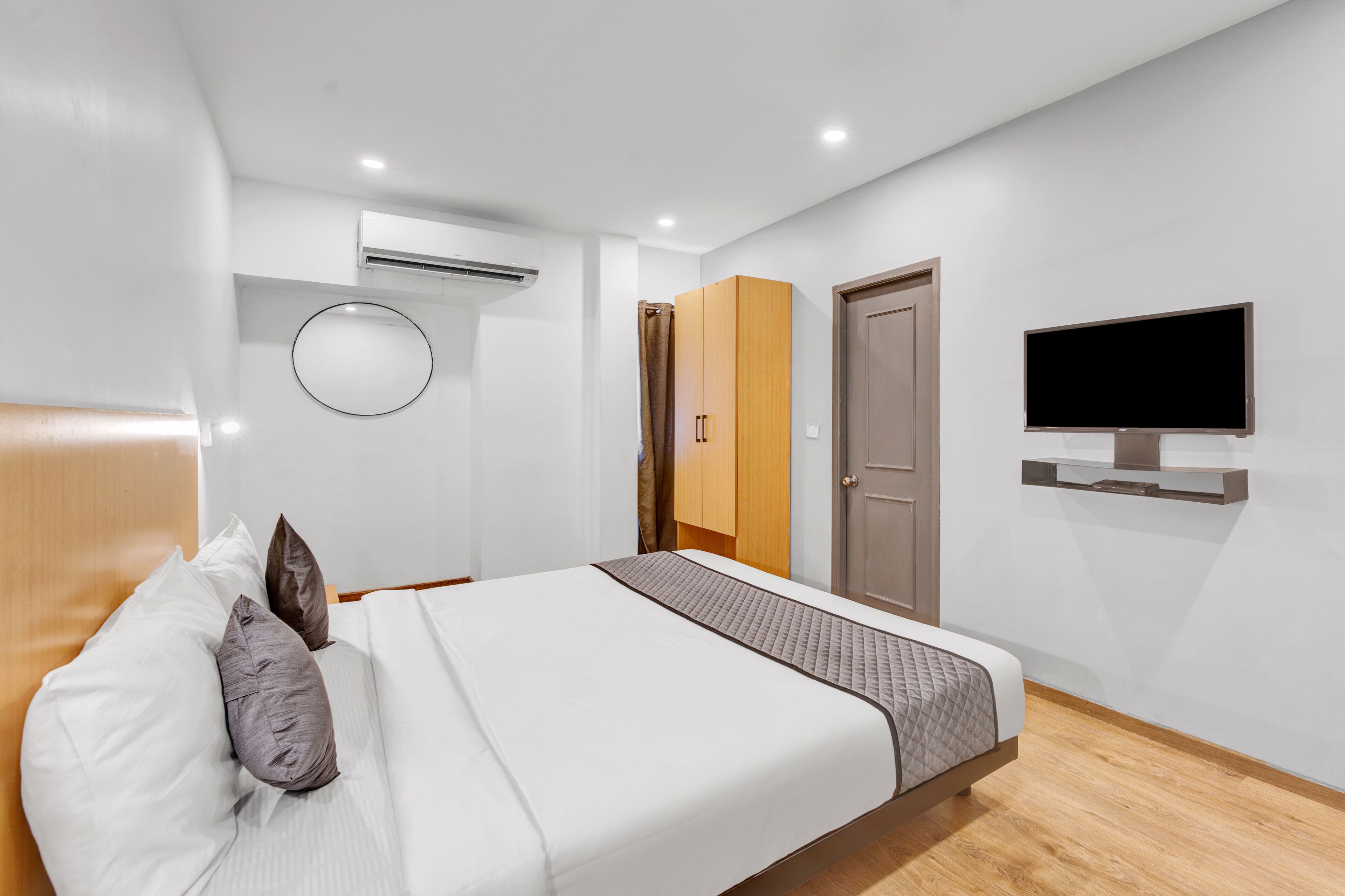 A modern hotel room with a large bed, a television mounted on the wall, and a wardrobe.
