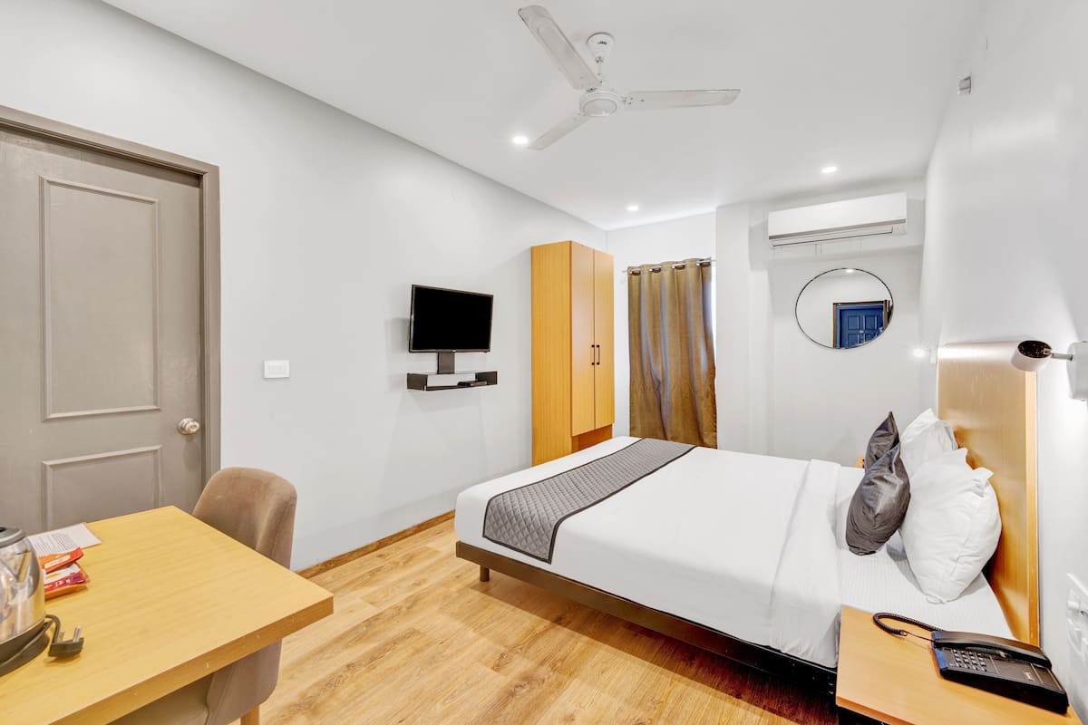 A hotel room with a bed, a desk, a television, a wardrobe, a ceiling fan, a mirror, and a bathroom door.
