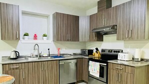 A modern kitchen with wooden cabinets, stainless steel appliances, and a window with decorative items. - Stylish, clean&cozy new 2 bedroom guest suite (Abbotsford)