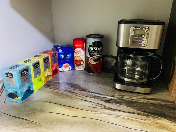 Kahvinkeitin, paketti Nescafe-kahvikapseleita, Tetley-teepakkaus ja useita Earl Grey -teepakkauksia keittiön työtasolla.