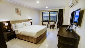 A hotel room with a large bed, a desk, a chair, a TV, and a window with a view. - AQABA COAST HOTEL (Aqaba)