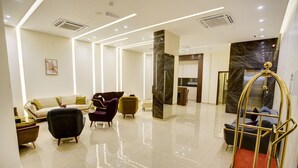 A spacious lobby with a modern design, featuring a sofa, armchairs, a marble column, and a gold elevator. - AQABA COAST HOTEL (Aqaba)