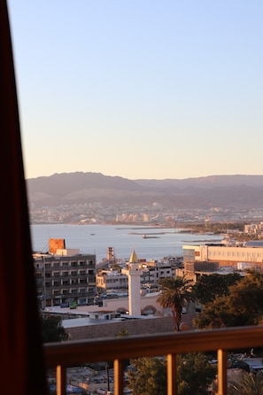 Une vue sur un paysage urbain côtier, avec un bâtiment imposant doté d’un dôme et d’une tour, prise depuis un balcon.