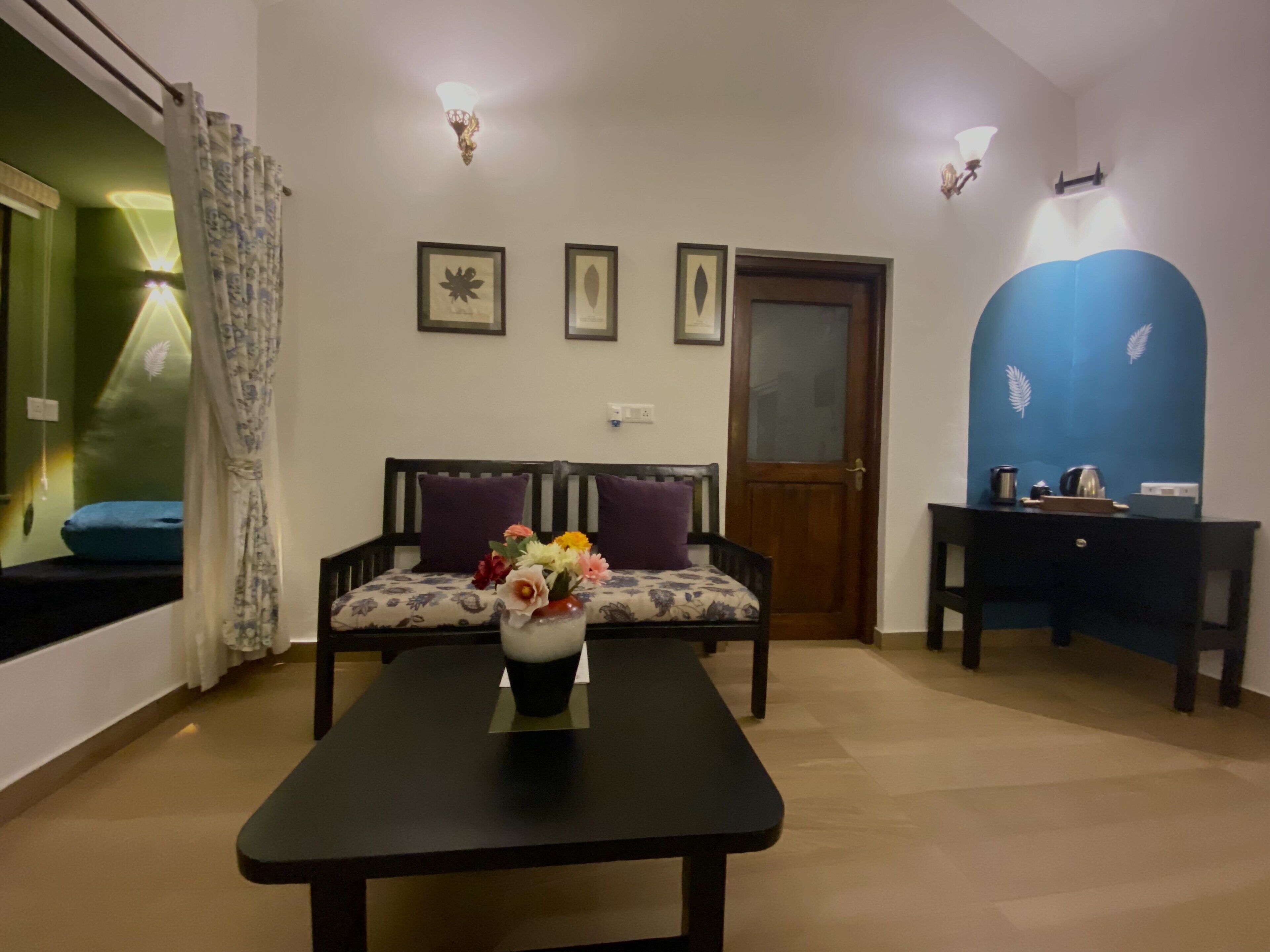 A room with a sofa, a table with a vase of flowers, a door, and wall-mounted lights.