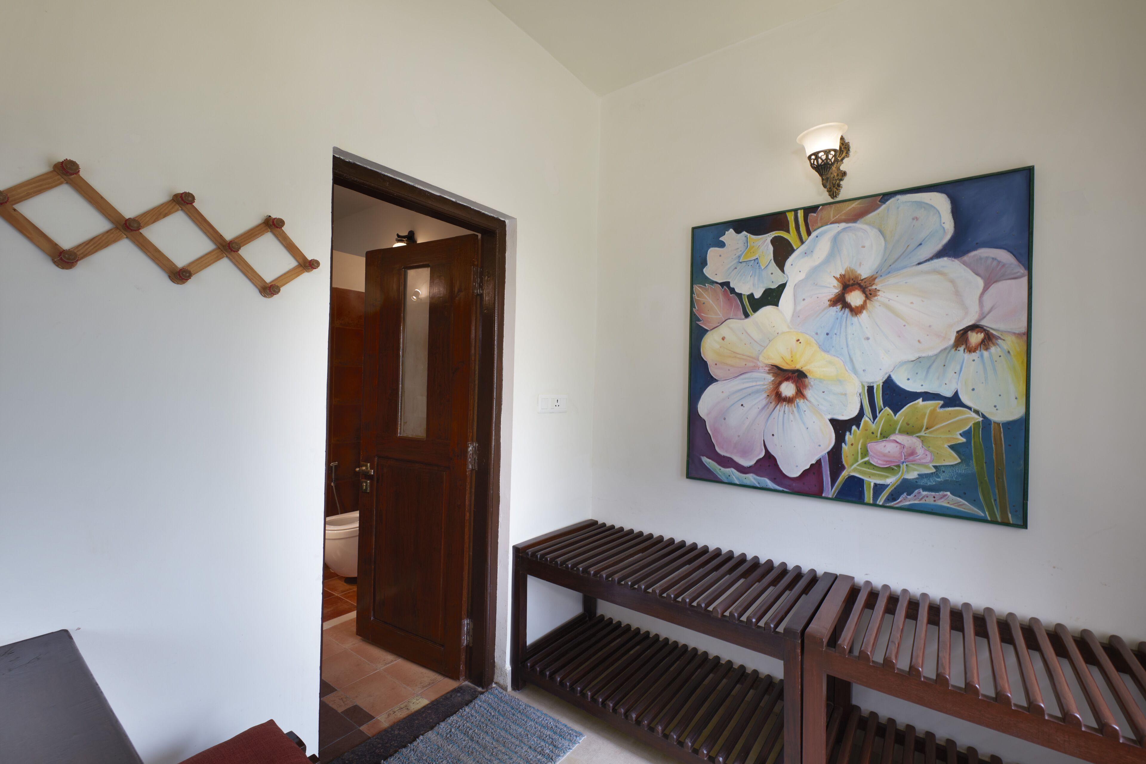 A hallway with a wooden bench, a door leading to a bathroom, and a floral painting on the wall.