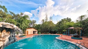 A swimming pool with a rock formation on one side, a small building, and a gazebo with string lights. - Tathastu Kanha (Baihar)