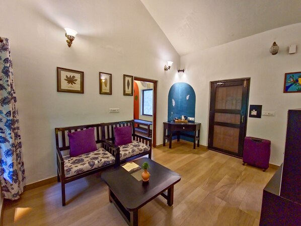A living room with a sofa, a coffee table, a small table with a lamp, and a door. - Tathastu Kanha (Baihar)