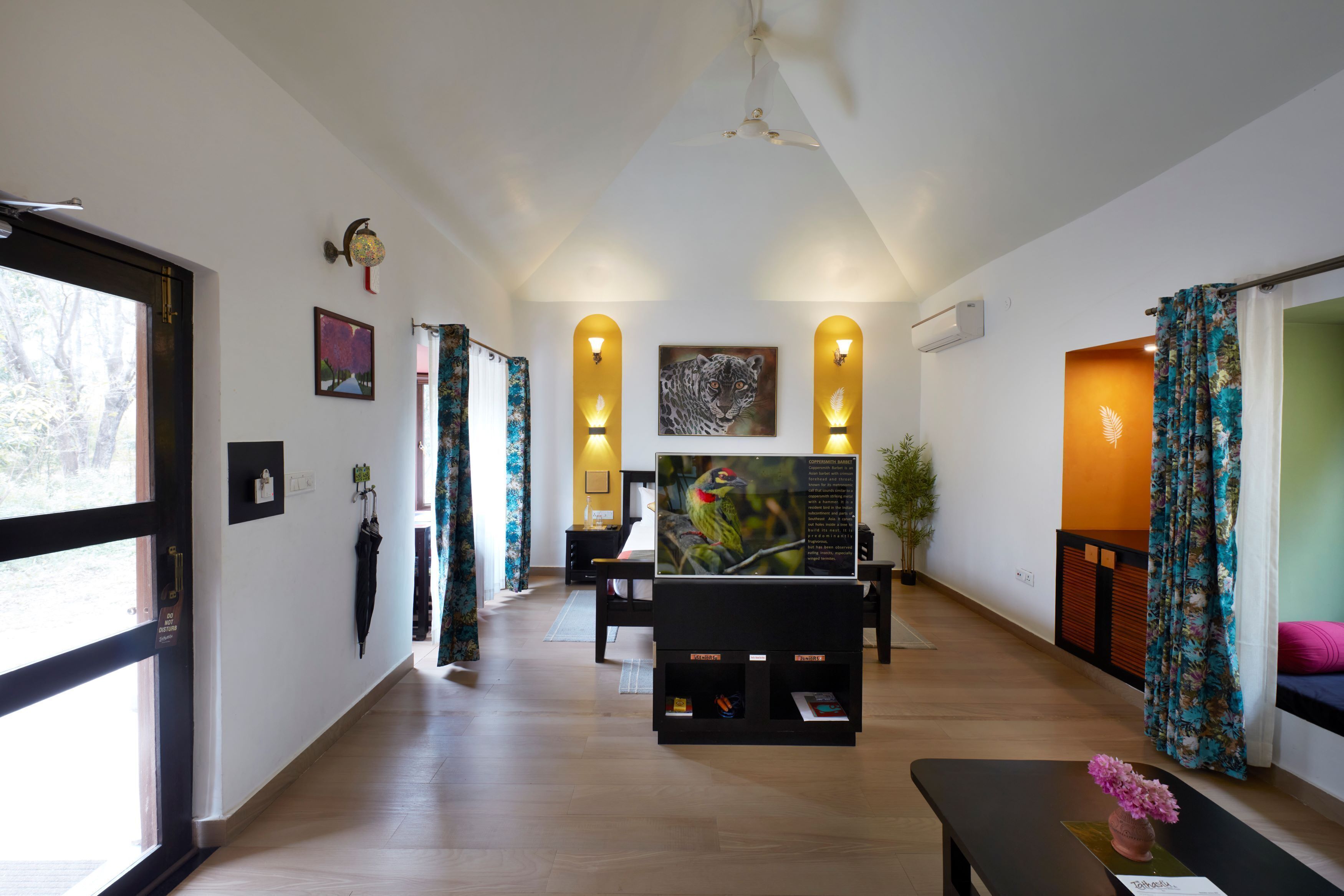 A spacious living area with a wooden floor, a flat-screen TV, and a seating area with a bench and a table.