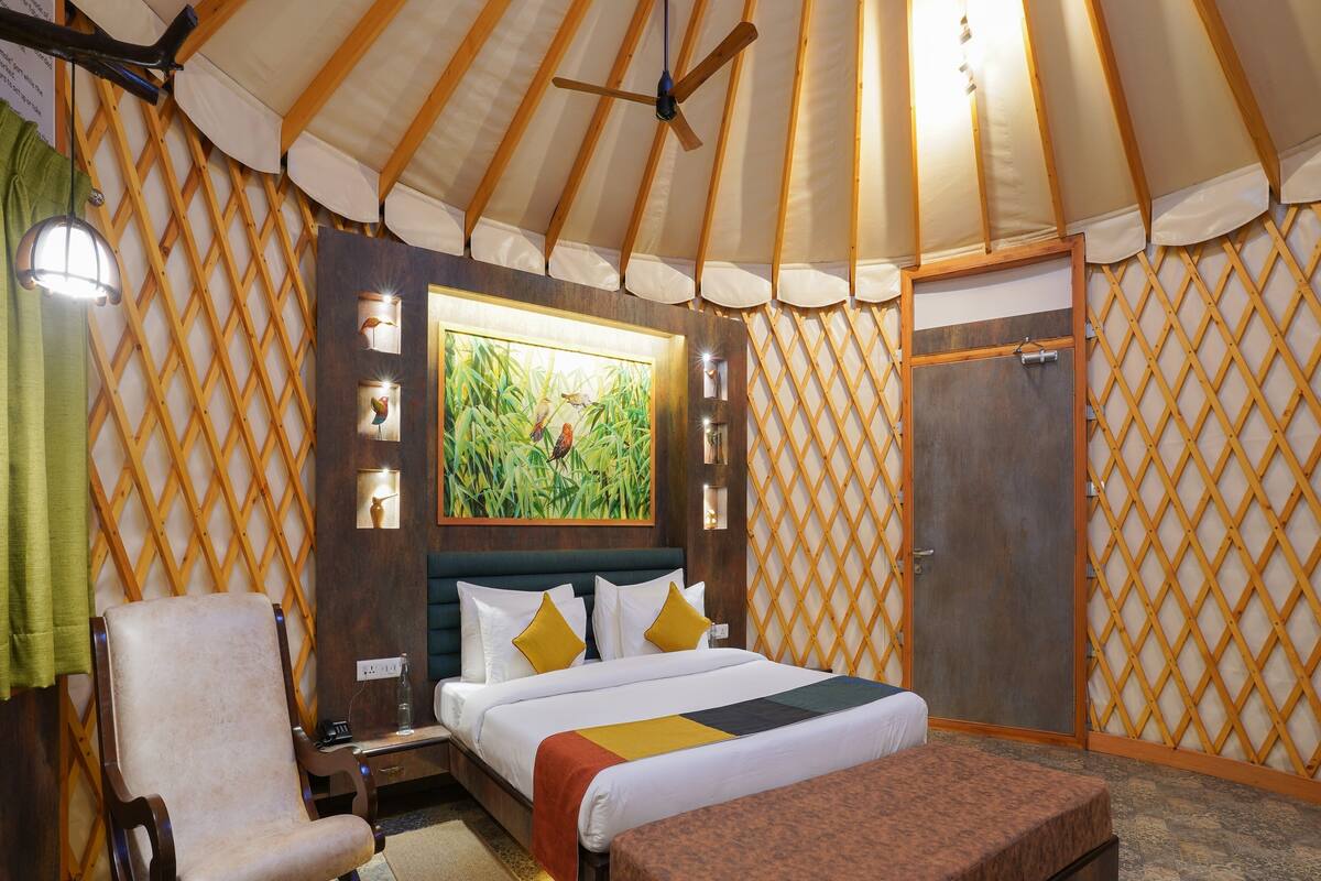 A room with a bed, a chair, a bench, a wooden door, and a window with a painting.