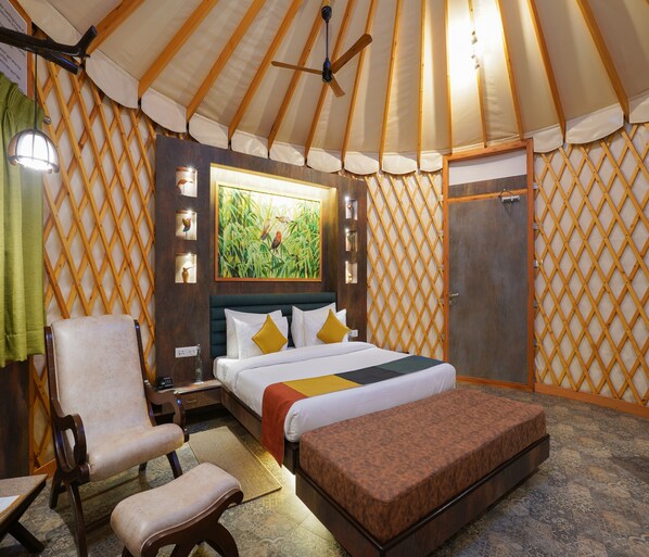 A room with a bed, a chair, a bench, a wooden door, and a window with a painting. - Tathastu Kanha (Baihar)