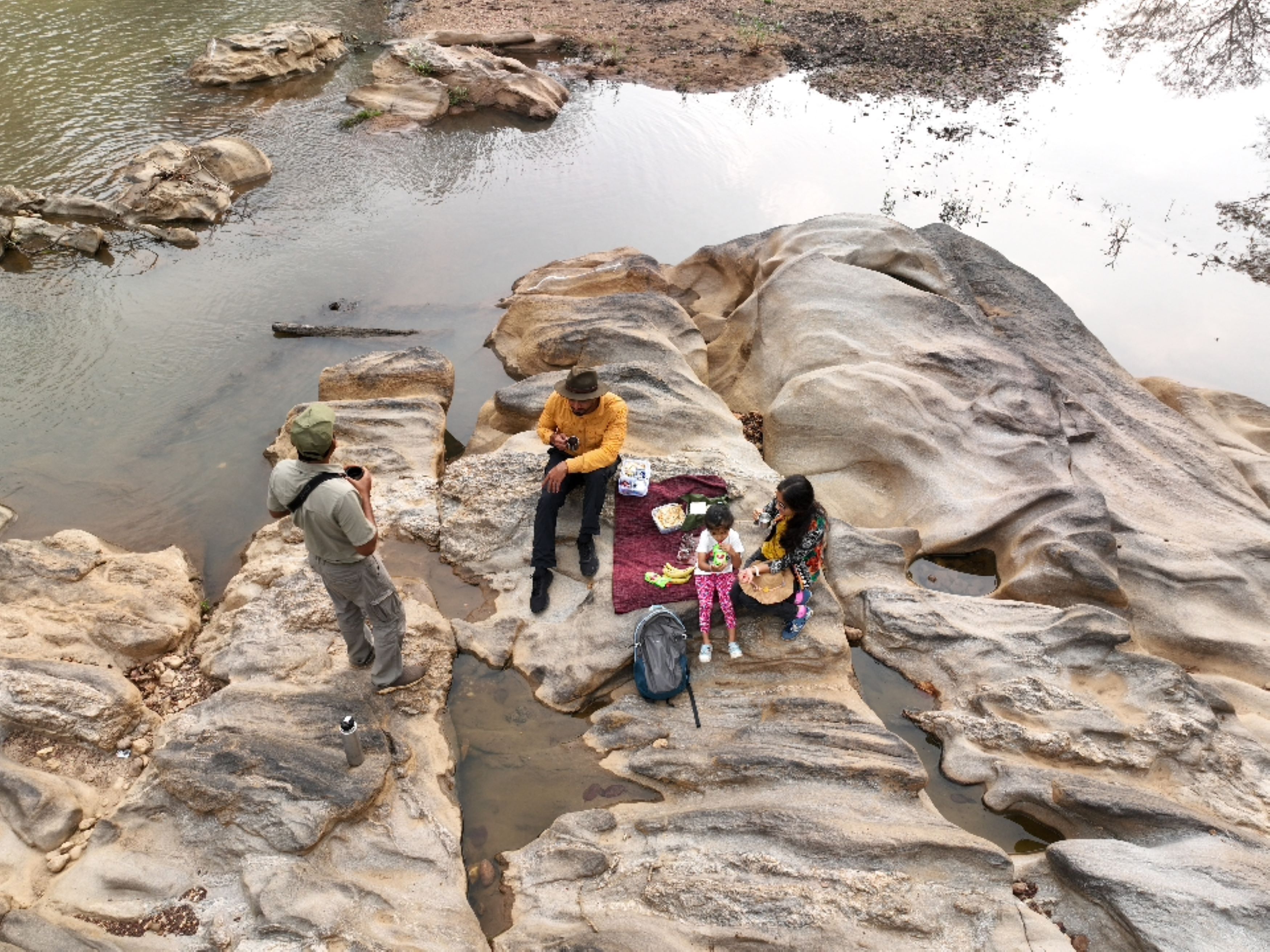Un groupe de personnes est assis sur un terrain rocheux, près d’une étendue d’eau.