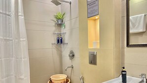 Casa de banho com chuveiro, sanita, lavatório e uma pequena prateleira com artigos de higiene pessoal.