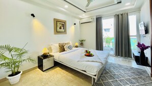 Quarto de hotel com cama, mesa de cabeceira, planta em vaso e ventoinha no teto.