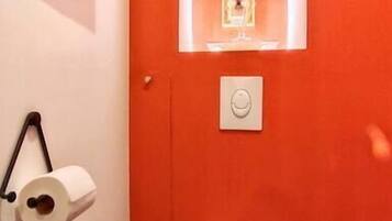 Une salle de bain avec des toilettes blanches, un rouleau de papier toilette, une œuvre d’art encadrée accrochée au mur et un mur d’accent de couleur rouge.