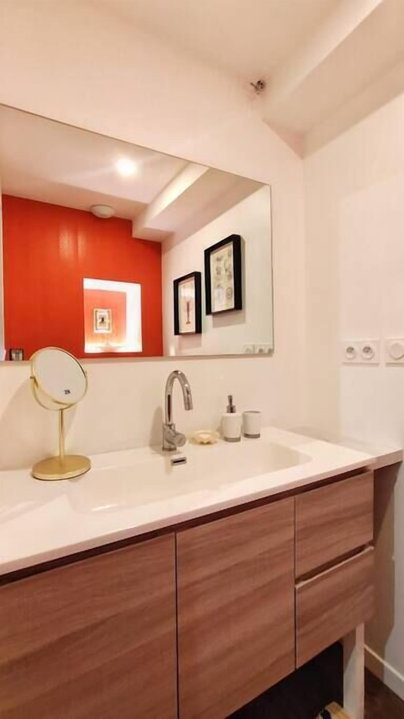 A bathroom with a white sink, a mirror, a red accent wall, and a framed picture above the mirror.