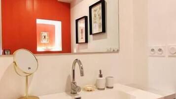 A bathroom with a white sink, a mirror, a red accent wall, and a framed picture above the mirror.