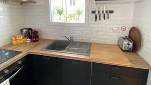 Moderni keittiö, jossa on puinen työtaso, mustat kaapit, ruostumattomasta teräksestä valmistettu pesuallas ja ikkuna, josta avautuu näkymä vehreään maisemaan.