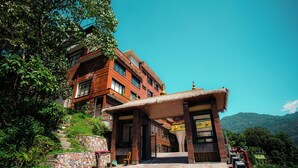 A multi-story building with a stone facade, a thatched roof entrance, and a paved pathway leading to the entrance. - Oro Montana Hotels and Resort (Gangtok)
