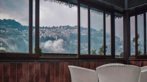 A room with a view of a mountainous landscape through large windows. There are two white wicker chairs in the foreground. - Oro Montana Hotels and Resort (Gangtok)