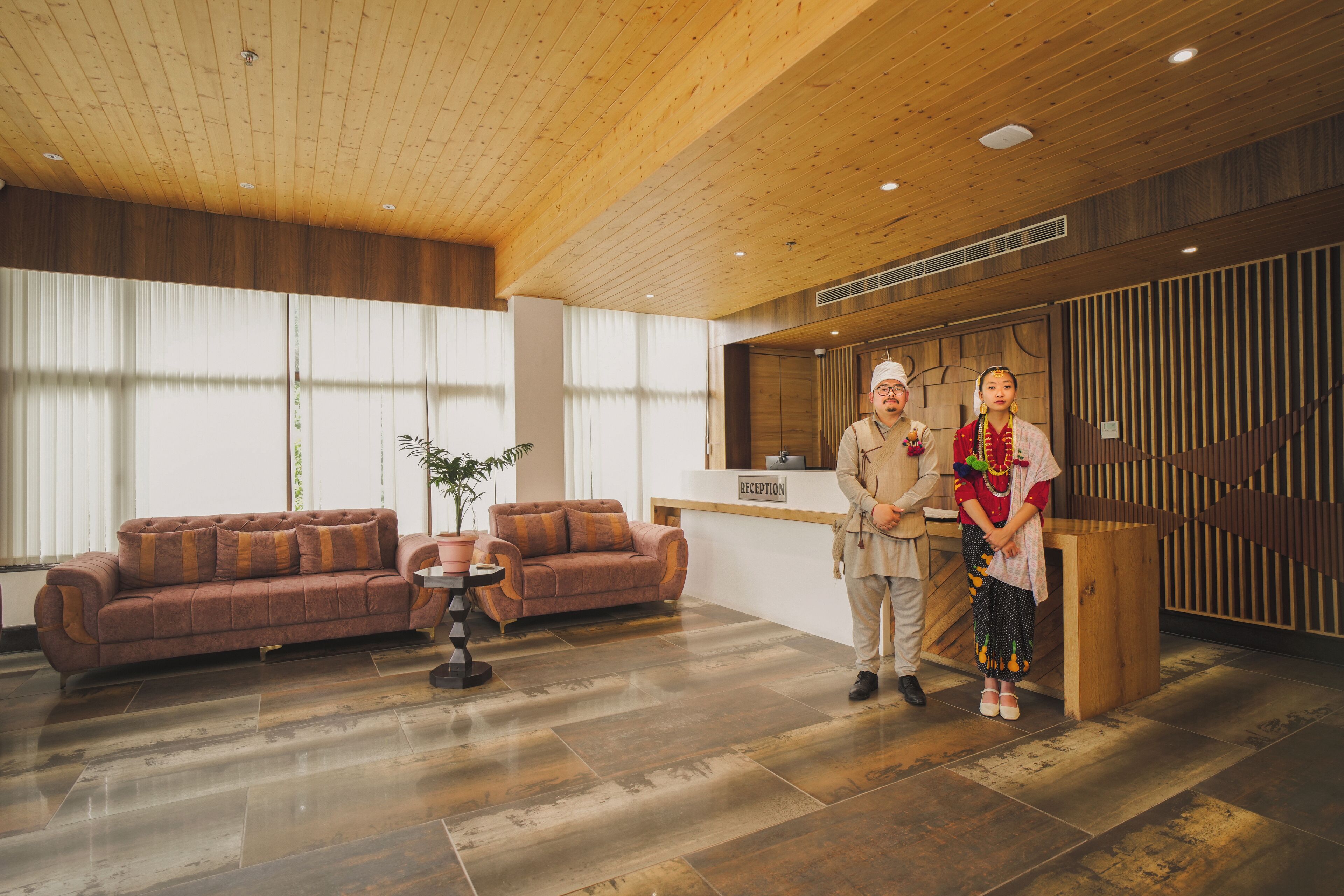 A reception area with a wooden ceiling, a reception desk, a brown sofa, and a potted plant.