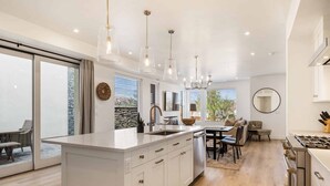 A modern kitchen with a central island, pendant lighting, and a dining area with a sofa and chairs. - Waters Edge by RedAwning (St. George)