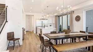 A modern kitchen with white cabinets, a stainless steel refrigerator, and a dining area with a wooden table and chairs. - Waters Edge by RedAwning (St. George)