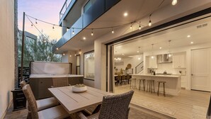 An outdoor dining area with wicker chairs and a table, a hot tub, and string lights. - Waters Edge by RedAwning (St. George)