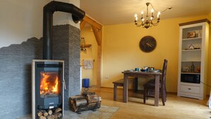 Een gezellige kamer met een stenen openhaard, een eettafel met stoelen, een kroonluchter en een klok aan de muur.