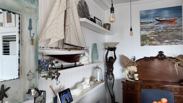Una habitación con un velero en miniatura, un cuadro de un barco y un florero sobre las estanterías.
