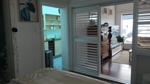 Una habitación con una cama, una puerta corrediza que da a una cocina y vistas a coches aparcados fuera.