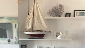 Un rincón comedor con una mesa redonda y dos sillas, un modelo de velero y objetos decorativos en estantes.