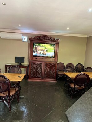 A dining area with a television mounted on a wooden cabinet, surrounded by wooden tables and chairs.
